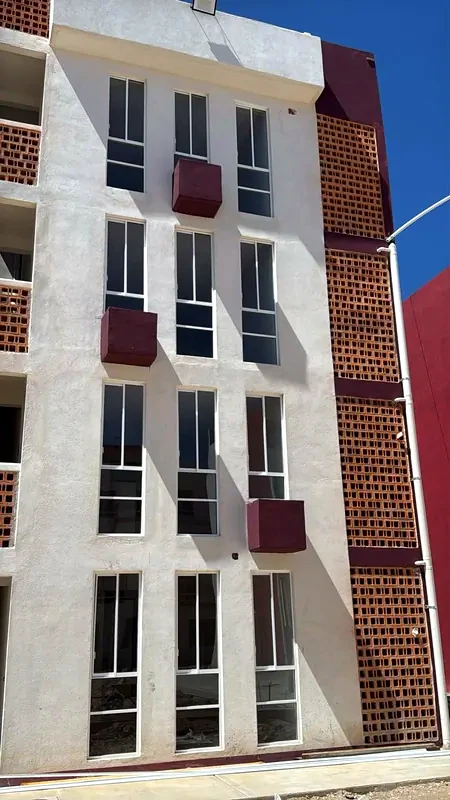 Fachada vertical blanca con ventanas altas, cajas en color vino y celosía de ladrillo