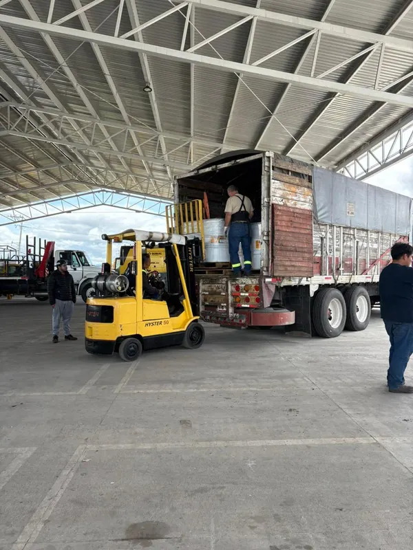 Montacargas y trabajadores cargando tambos en un camión